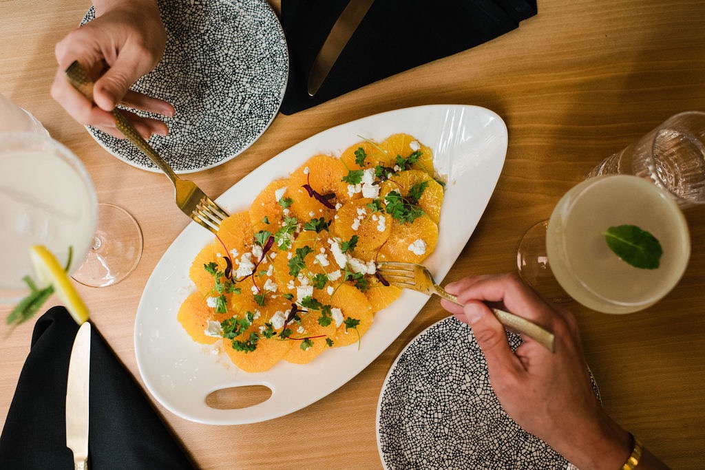 Two people pick at a plate of sliced fruits.