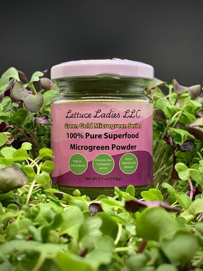 A jar of Lettuce Ladies microgreen powder sits amongst small microgreen sprouts. 