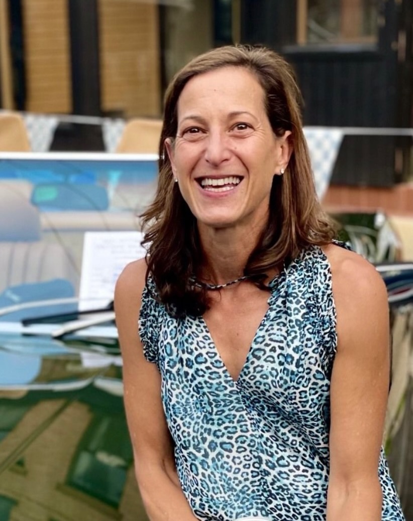 A woman in a blue cheetah top with long hair leaning against a car.