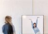Lolo y Lauti’s ‘Triple Threat’ Opens at the Mattress Factory A person stands in front of a barre bar as another person poses on a screen behind it.