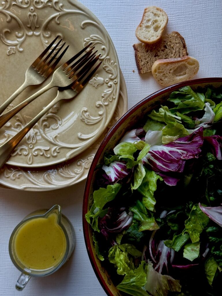Two plates sit beside a big bowl of salad with a measuring cup of yellow dressing below it.