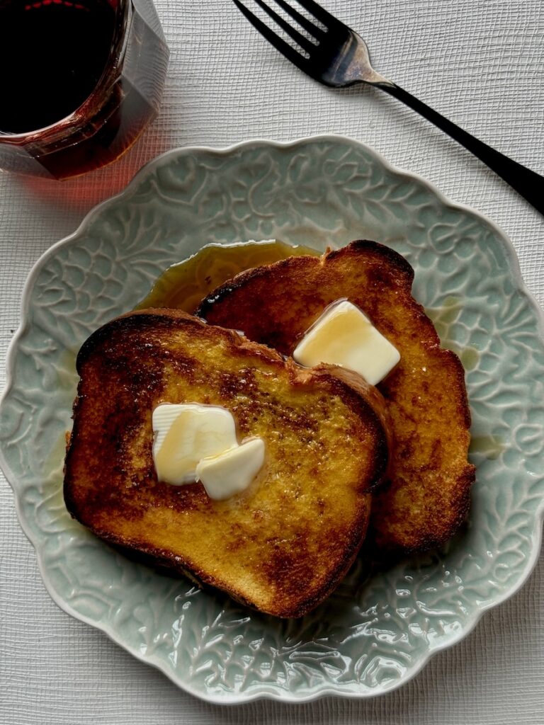 A stack of orange french toast on a green plate with butter and syrup on top.