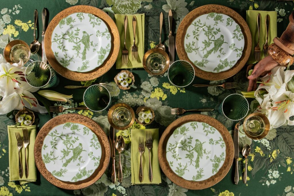A table full of four green and white plates with birds on them, green napkins, and gold silverware.