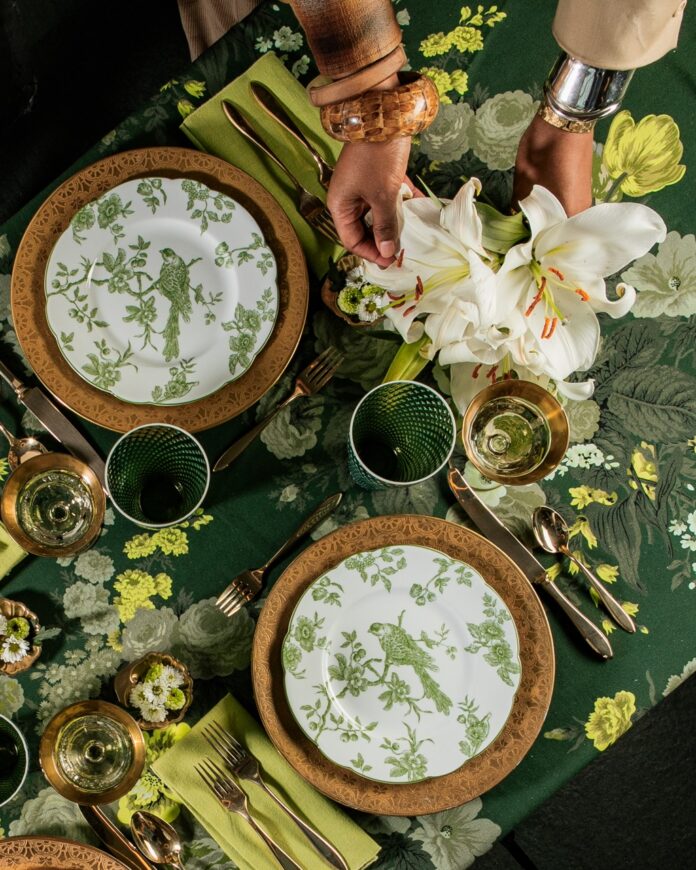 A woman's hands fix flowers in a vase on a table setting of green and gold.