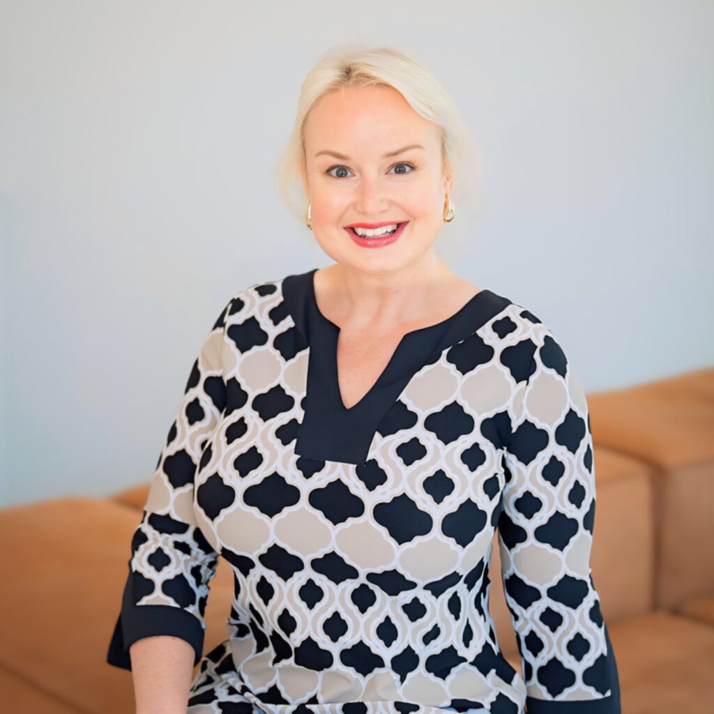 A woman in a whit eand black sweater with short blonde hair.
