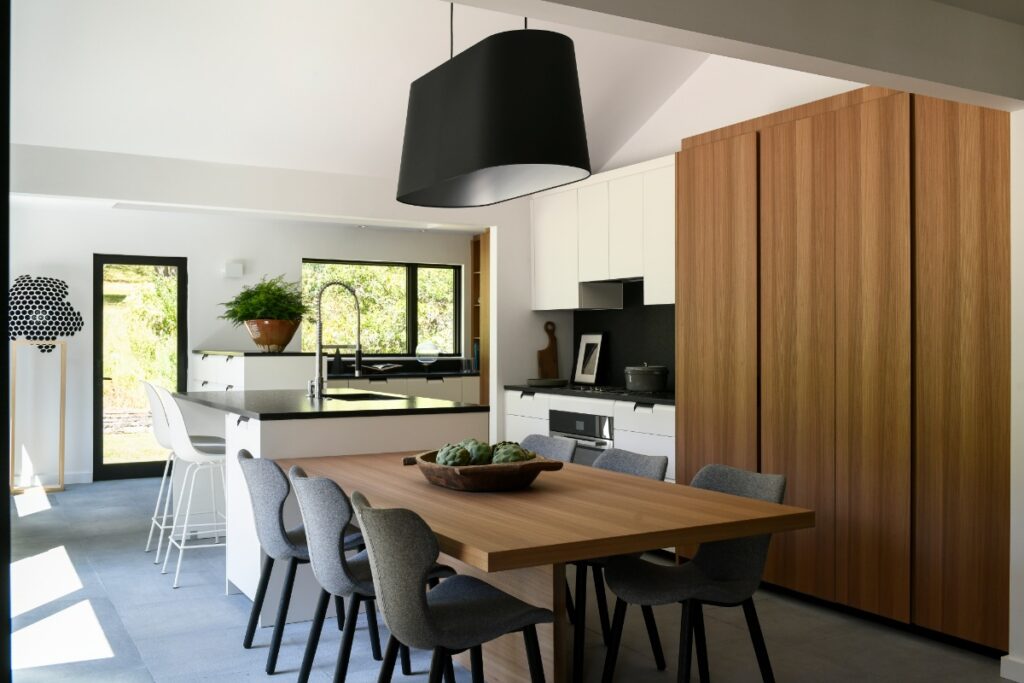 A minimalist Poliform kitchen in Fox Chapel featuring an elm wood dining table, sculptural grey B&B Italia chairs, a black architectural light fixture, and sleek white cabinetry.