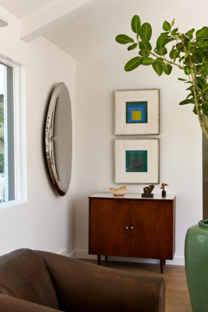 A maximalist Squirrel Hill bedroom featuring bold large-scale botanical wallpaper, a blue-patterned headboard, and a grey nightstand with a hanging gold pendant lamp.