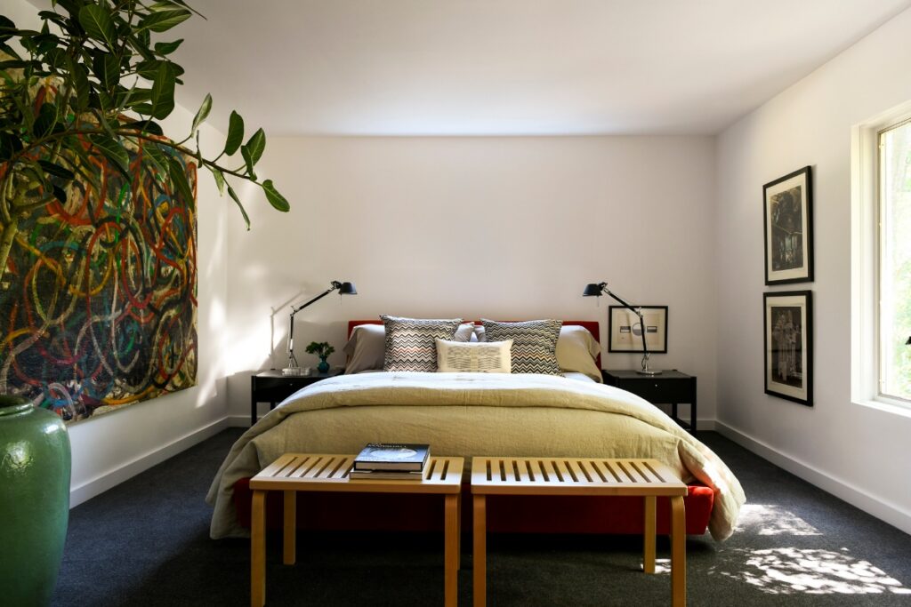 A serene primary bedroom in Fox Chapel featuring a large-scale Abstract Expressionist painting, and a pair of light wood slatted benches.