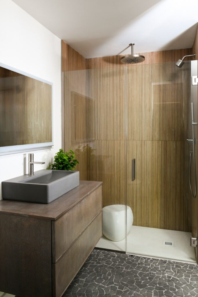 A primary bathroom in Fox Chapel featuring organic wood-look porcelain shower tiles, a mosaic lava stone floor, a concrete vessel sink, and a frameless glass shower.