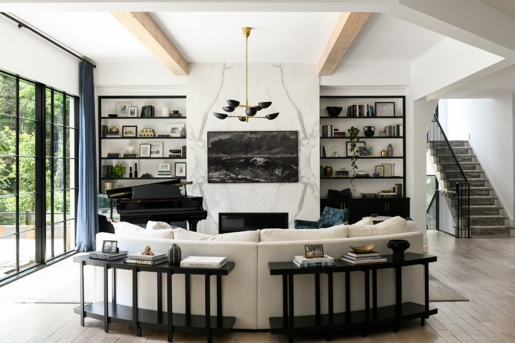 A cozy, modern living room corner in a Fox Chapel home featuring a white curved sofa, a marble fireplace with a large abstract painting above it, and a grand piano.