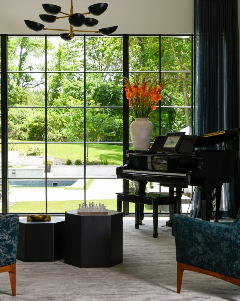 A sun-drenched modern living room in Fox Chapel featuring floor-to-ceiling black windows, a cream sectional sofa, and a sculptural white petal chandelier designed by Elysa Roberts Interiors.