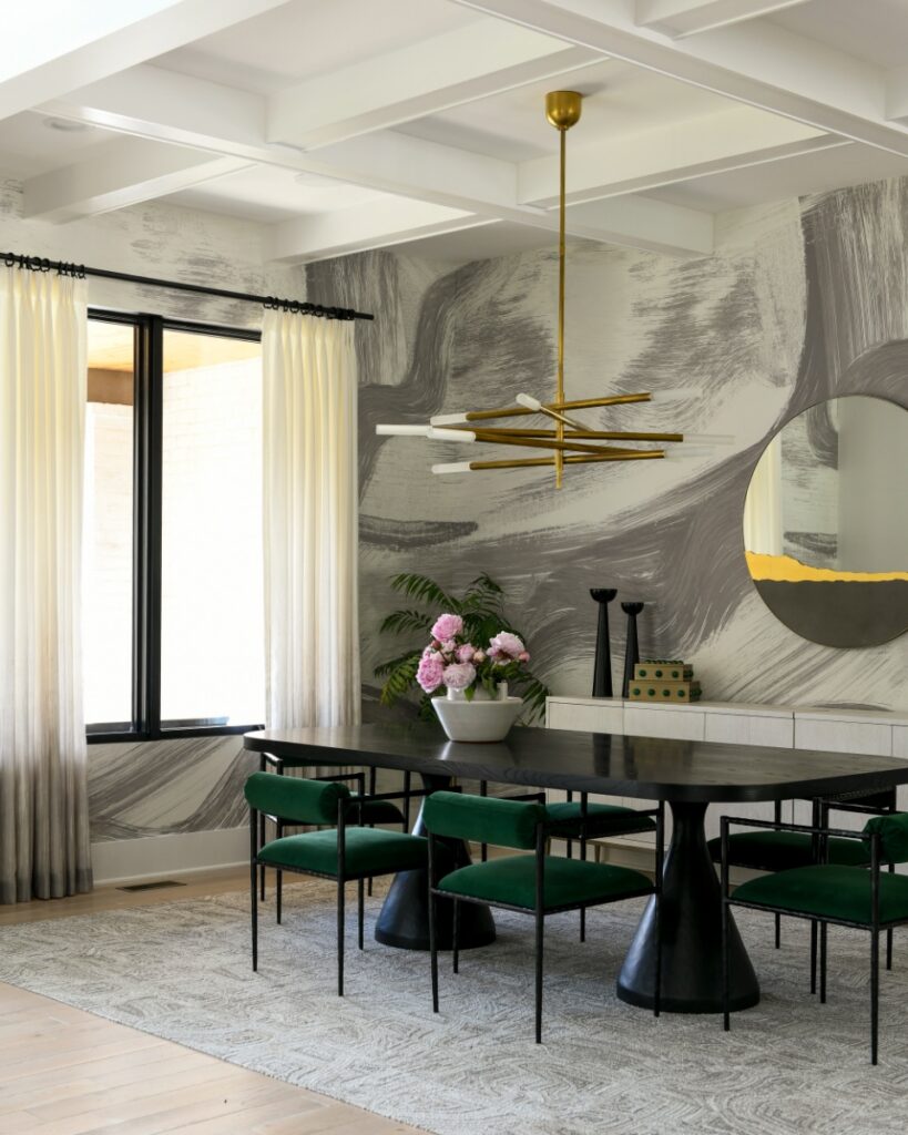 A sophisticated Fox Chapel dining room featuring an oval black table, green velvet chairs, a gold branch-style chandelier, and abstract grey brushstroke wallpaper.
