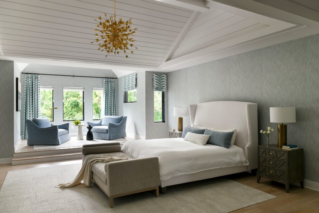 A serene light-blue primary bedroom in a Fox Chapel home featuring a vaulted white-paneled ceiling, a cream wingback bed, and a gold starburst chandelier.