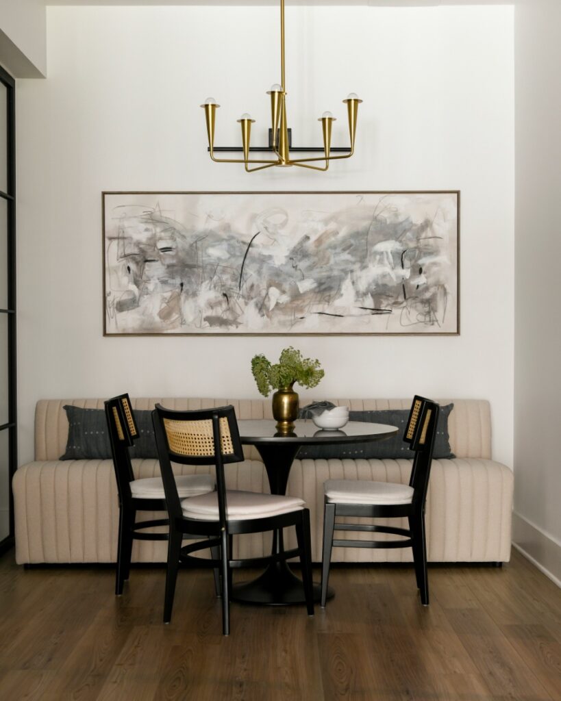 A sophisticated dining nook in a Fox Chapel residence featuring a black pedestal table, cane-back chairs, a fluted neutral banquette, and a modern gold chandelier, designed by Elysa Roberts Interiors.