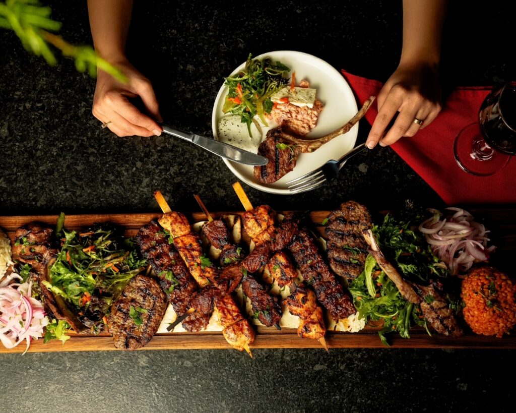 A large Mediterranean mezze platter from AVVA in Aspinwall featuring grilled lamb chops, chicken skewers, and kofte served with fresh greens and red onion.