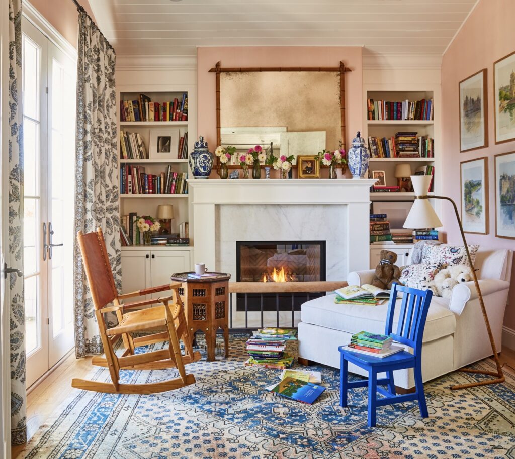 A brown rocking chair sits by a fire along with a white chair and a small blue wooden chair.