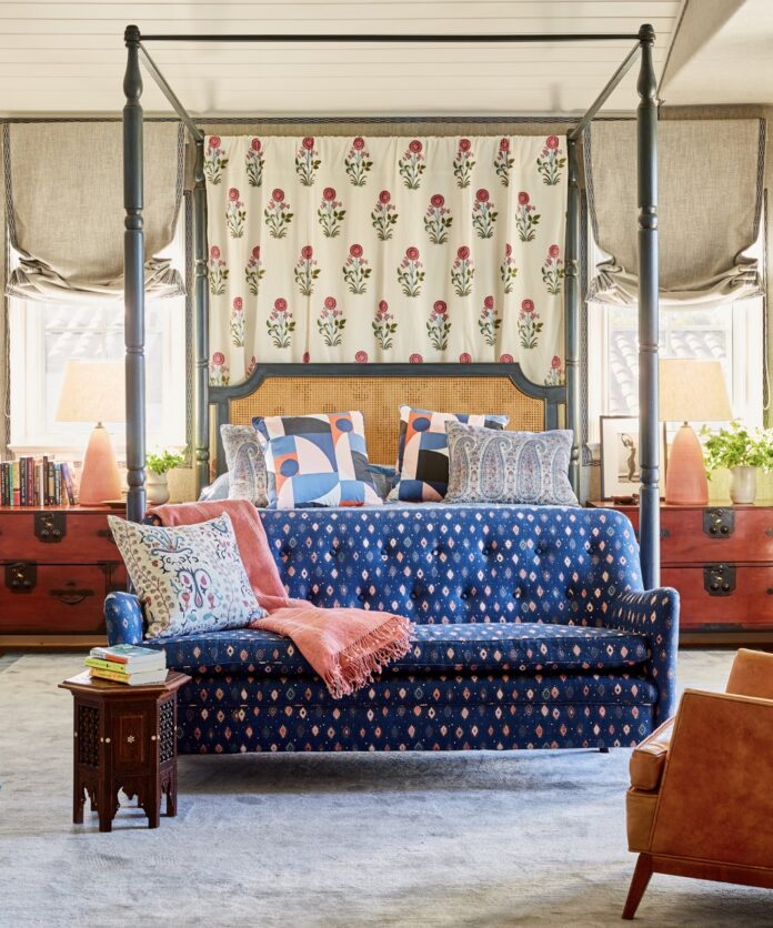 A blue couch sits at the end of a large four poster bed,