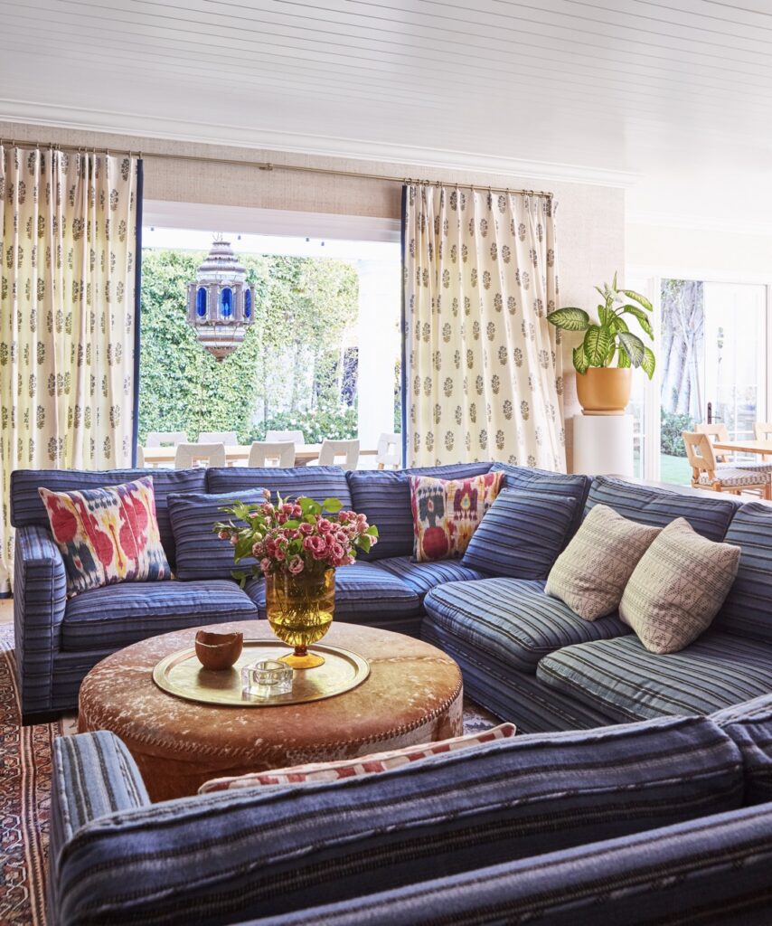A large blue rectangular sectional sits in front of bright curtains.