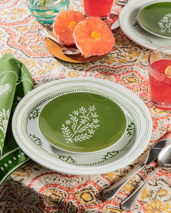 A white plate has a green painted plate on top of it with a green napkin to the left.