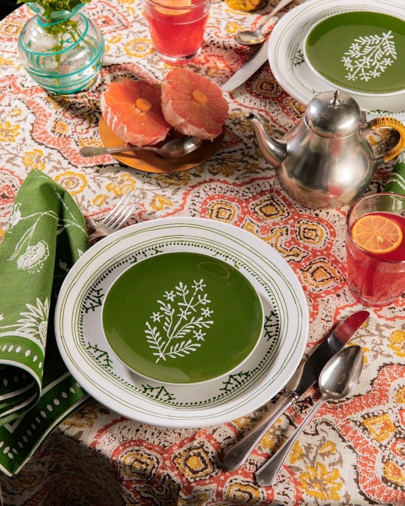 A table setting with green dinnerware on a busy orange pattern table cloth.