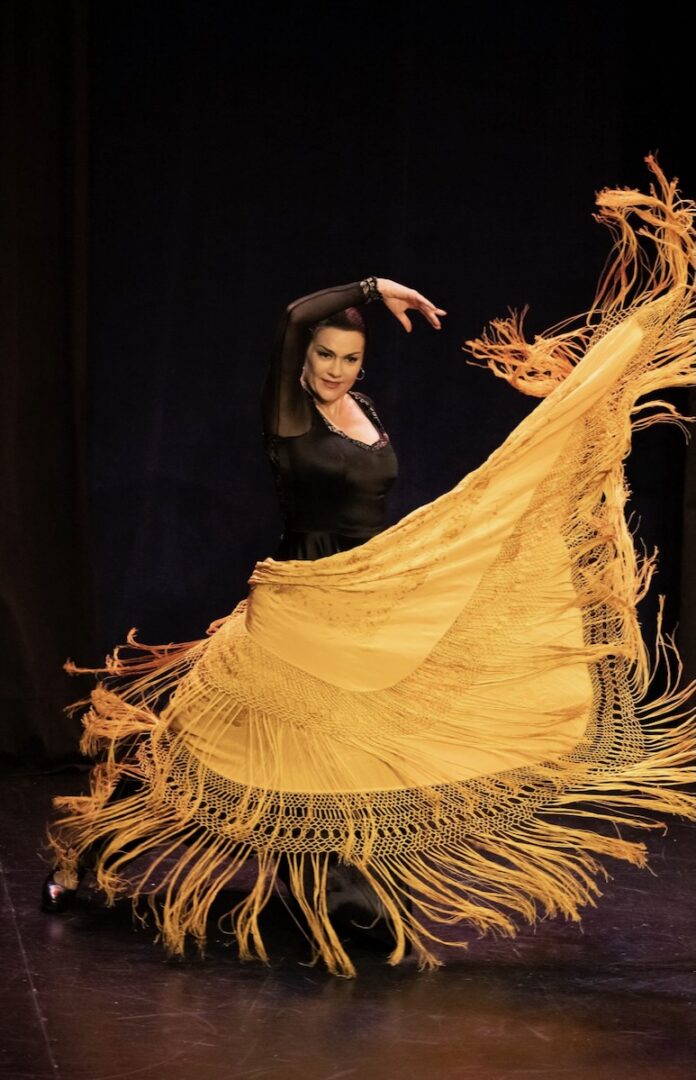A woman in a yellow dress performing a Flamenco dance on stage.