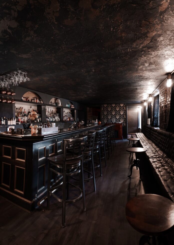 The inside of a Pittsburgh speakeasy with a lowkey bar and booth seating along the wall.