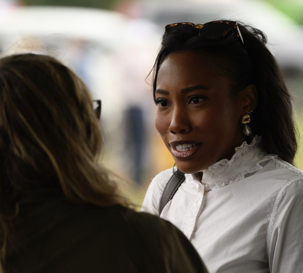 A woman in a white top and sunglasses on her head speaks to another.