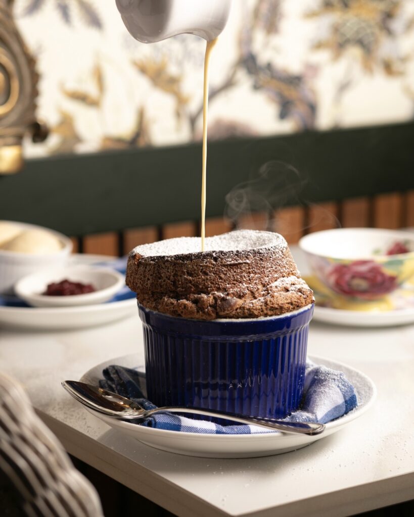 Poulet Bleu pours a hot syrup over a Chocolate Soufflé on a table.