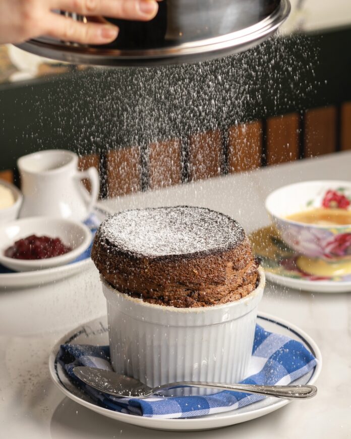 A chocolate Soufflé gets powdered sugar sprinkled over top.