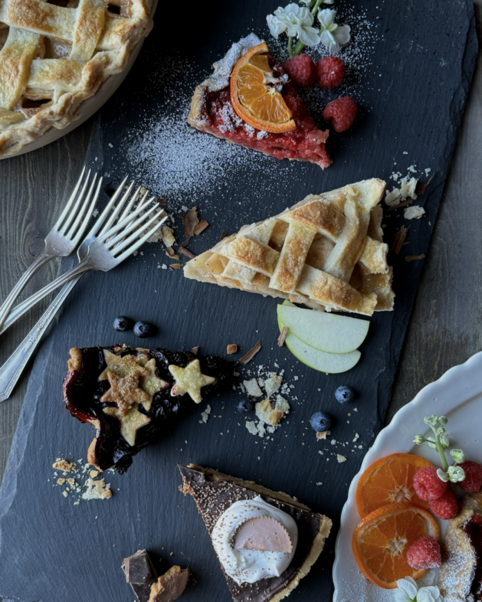 Four different slices of pie recipes sit on a black table with two whole pies peaking out of the top left and bottom right corners.
