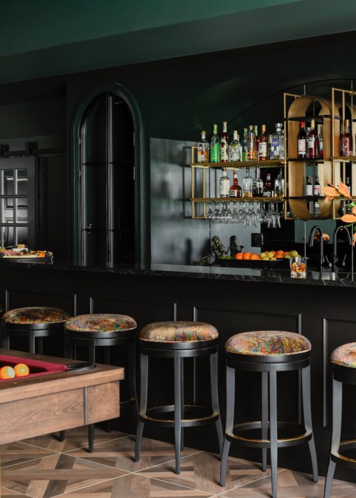 A bar area with stools sits behind the corner of a pool table with two yellow balls near the corner pocket.