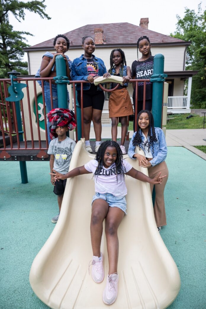 A group of diverse children smiling and posing on a playground slide in front of a house in South Park, Pennsylvania.