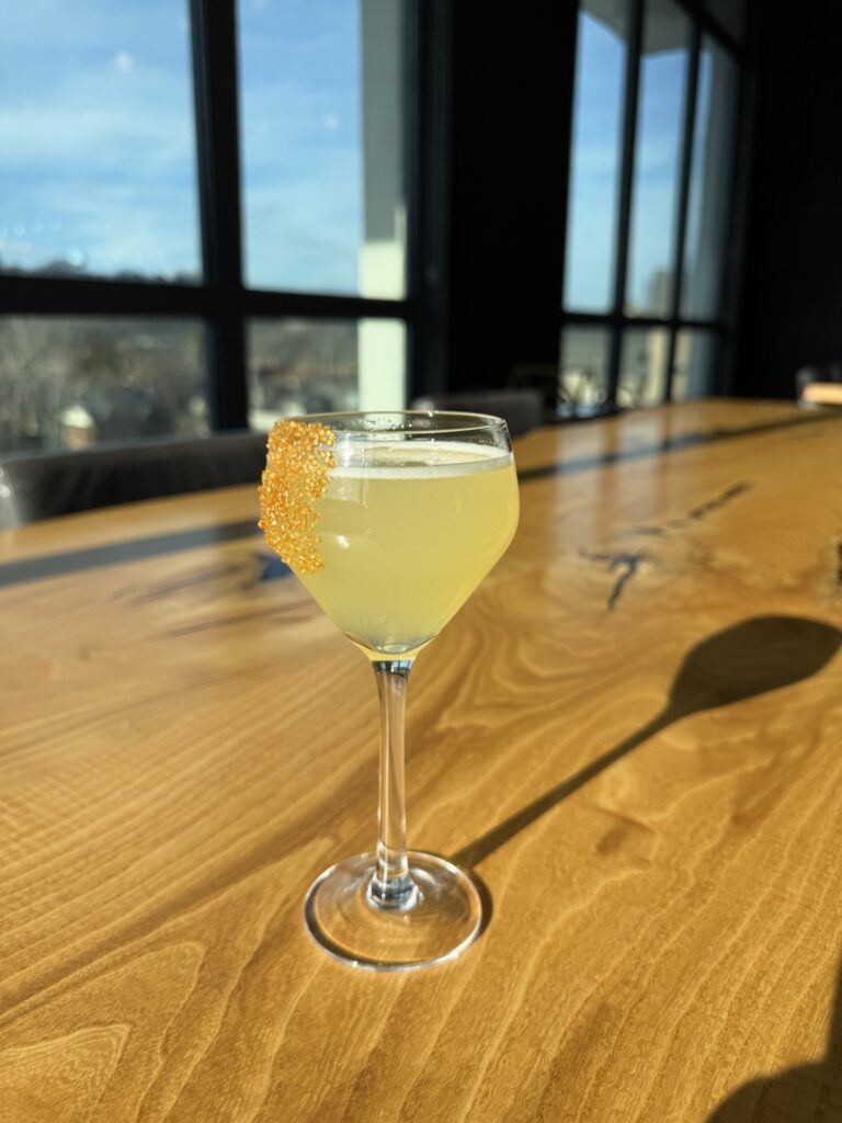 A yellow cocktail with gold sugar along the side of the glass. 