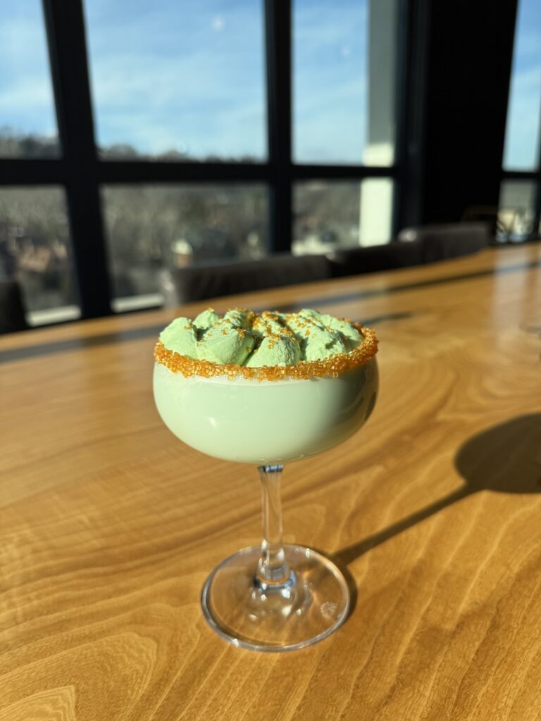 A green cocktail with a foam on top and gold rim.