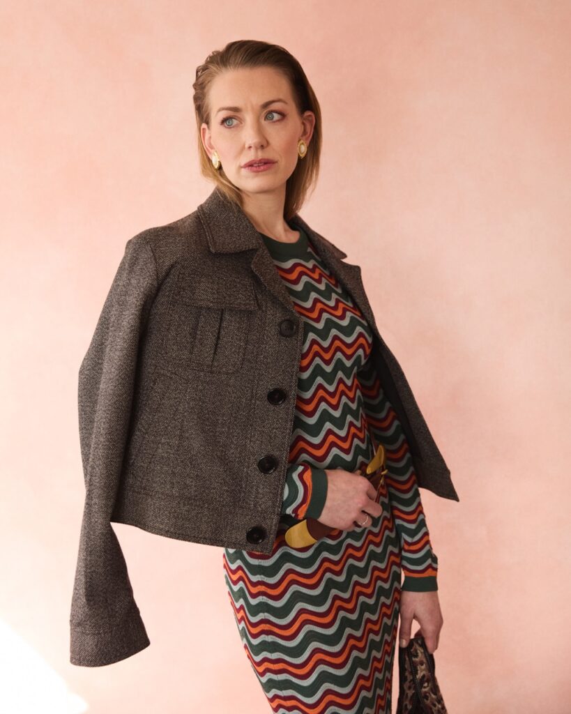 A woman in a dark leather jacket and zig-zag pattern dress.