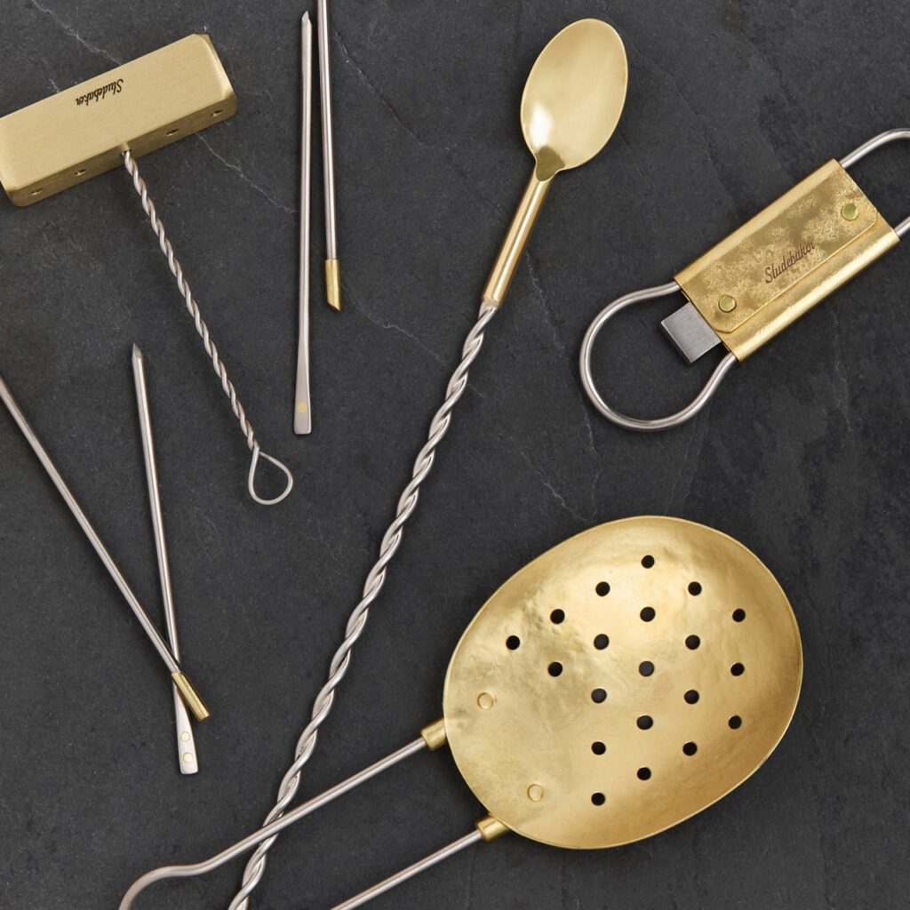 A gold metal cocktail kit with a strainer, bar spoon, bottle opener, and more.
