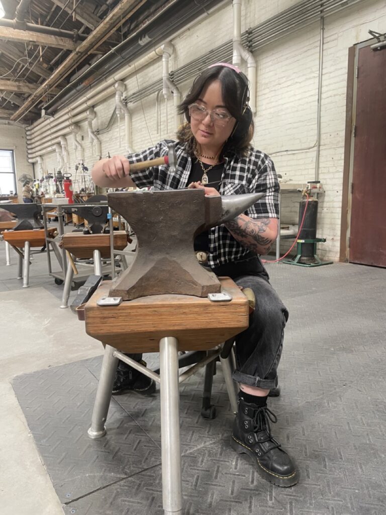 A woman hammers something on an anvil.