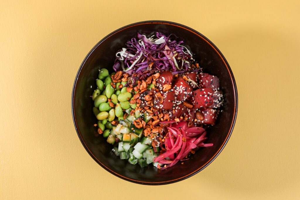 A black bowl full of slaws, seeds, and other veggies.