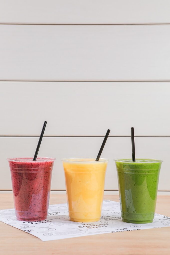 Three cups of smoothies in red, yellow, and green sit on a table.