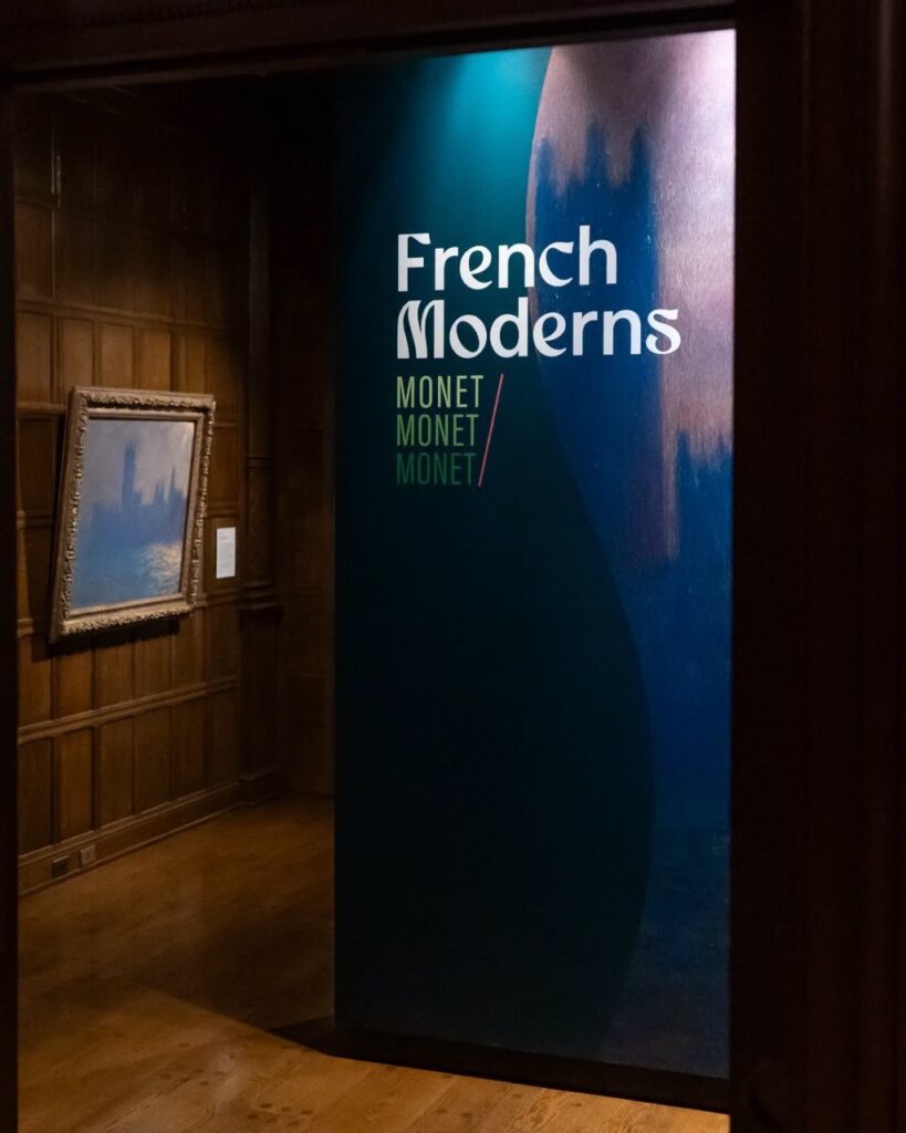 A sign for the French Moderns exhibit for Monet in front of a paintings on a museum wall.