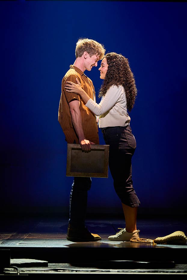 A man in a brown shirt and woman on a white shirt stand forehead to forehead.