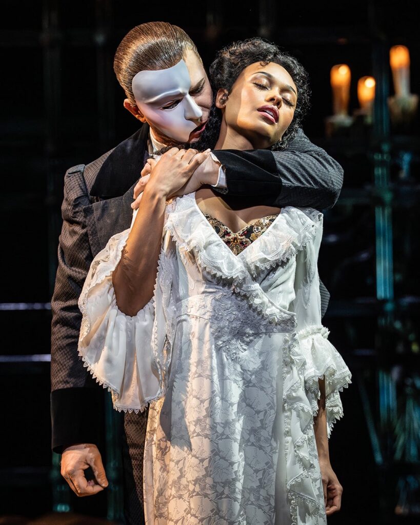The phantom holds Christine against him in her white dress.