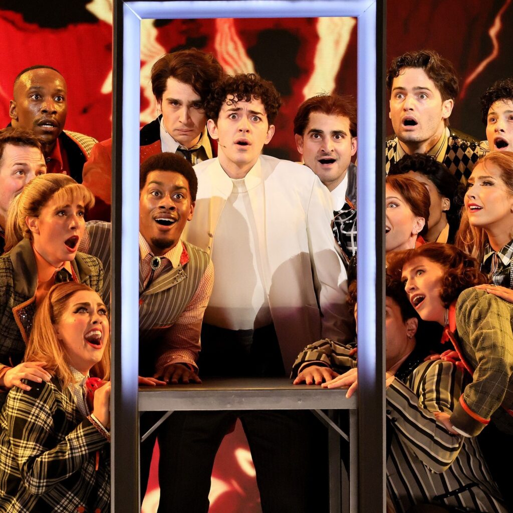 A group of actors in Tommy surround a rectangular frame.