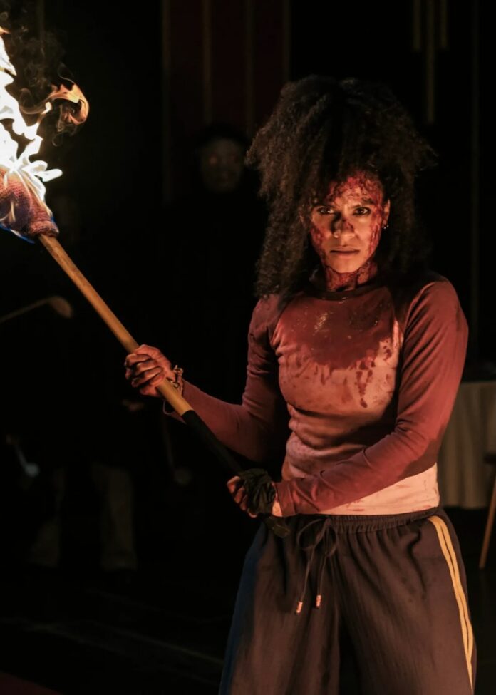 A woman covered in blood carries a torch.