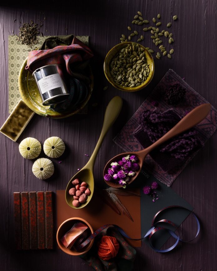 A series of spoons with carious small ingredients sit amongst other kitchen knick-knacks on a dark purple board.