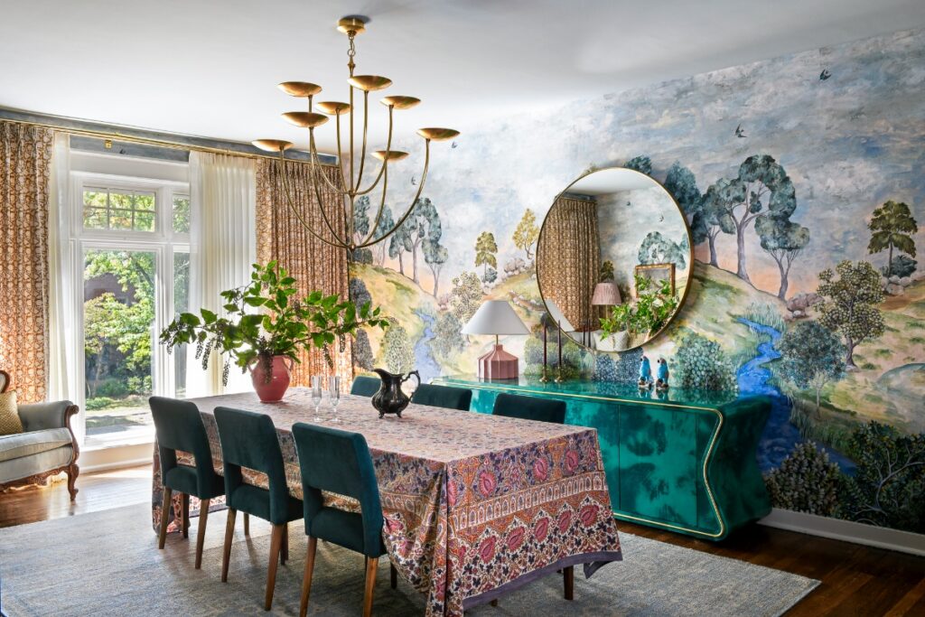 A sophisticated dining room designed by Michelle Gage featuring a vibrant Designers Guild forest mural, an emerald green Julian Chichester buffet, and a gold geometric chandelier.