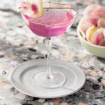 A tall pink martini cocktail with a watermelon radish on a tooth pick as a garnish.