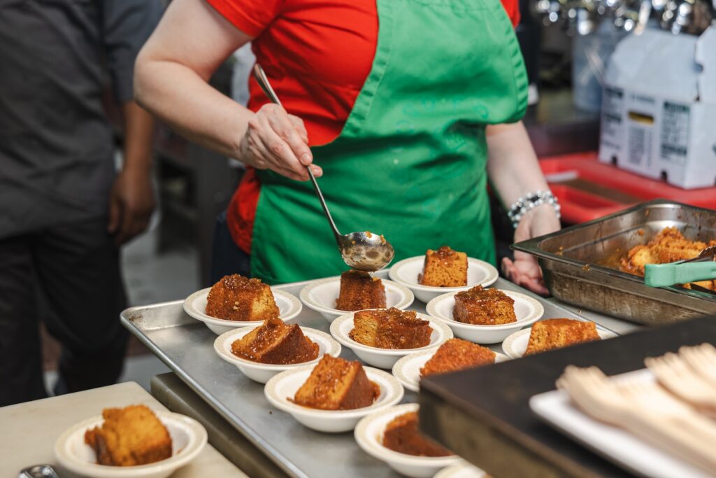 A women behind a counter finishing off individual small plates of food for an event for 412 food rescue.