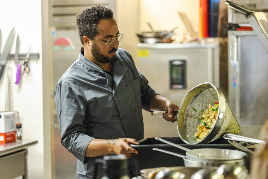 A chef in a blue chef coat preparing pasta.