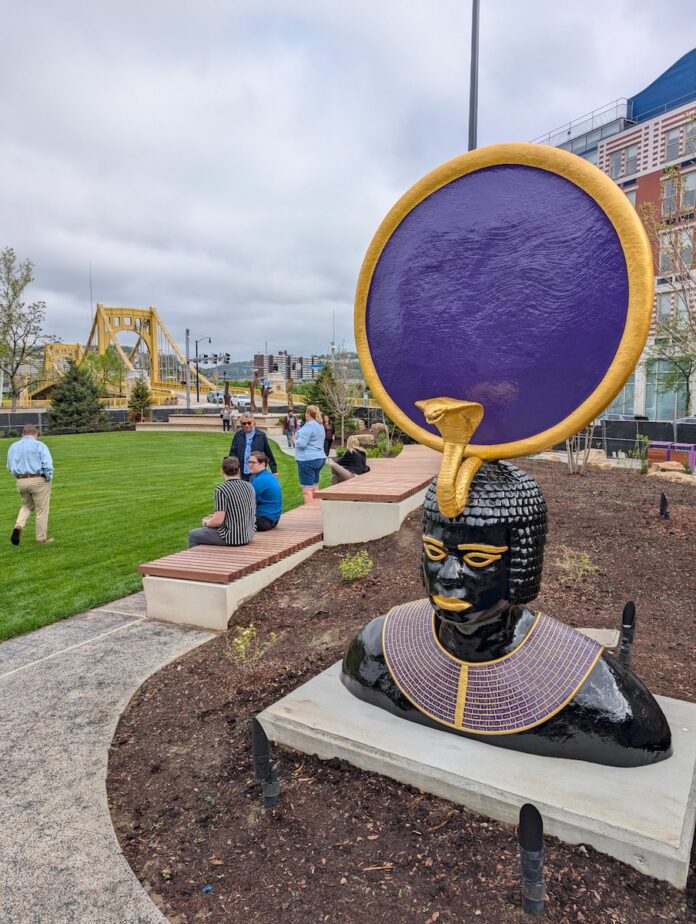 A large statue of a man with a snake and purple circle above his head sits in Arts Landing.